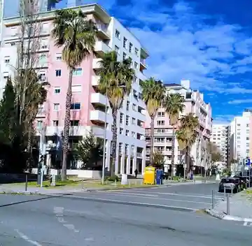 Rua residencial em Telheiras, Lisboa, com edifícios, passeio e estacionamento.